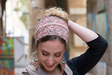 A woman wearing a White Rose lace headband with red and green floral embroidery, styled in a half-up bun, with a blurred outdoor background.