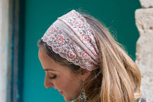 A woman wearing a light pink and white floral lace headband, shown in profile against a teal door background.