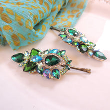 Decorative hair pins with green gemstones on a patterned fabric background

