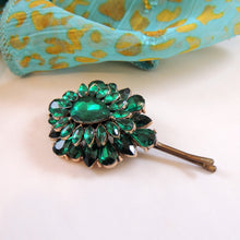 Green gemstone brooch on a white surface with a patterned fabric in the background

