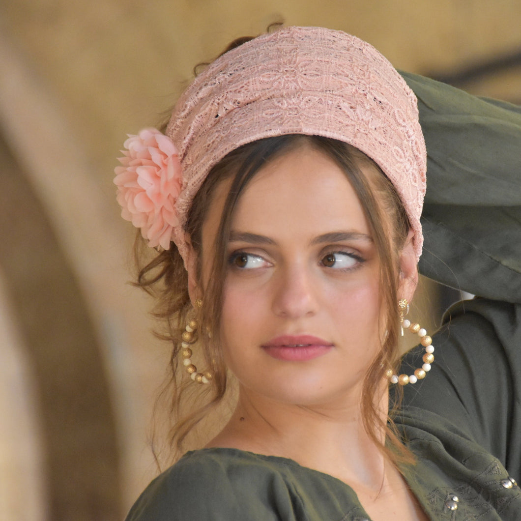 Woman wearing a pink lace headband with a flower and matching earrings.