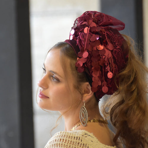 Woman wearing a decorative red headpiece with sequins, looking to the side.

