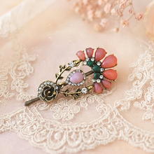 Vintage-style brooch with pink and green stones on a lace background

