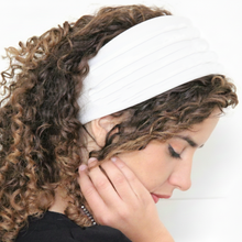 Woman wearing a white headband with curly hair on a plain background

