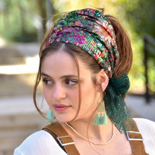 Woman wearing a colorful headscarf and green earrings outdoors

