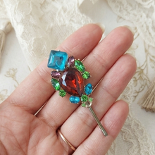 Colorful gemstone brooch held between fingers on a lace background


