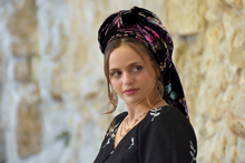 Woman wearing a colorful headscarf and black top with a blurred natural background

